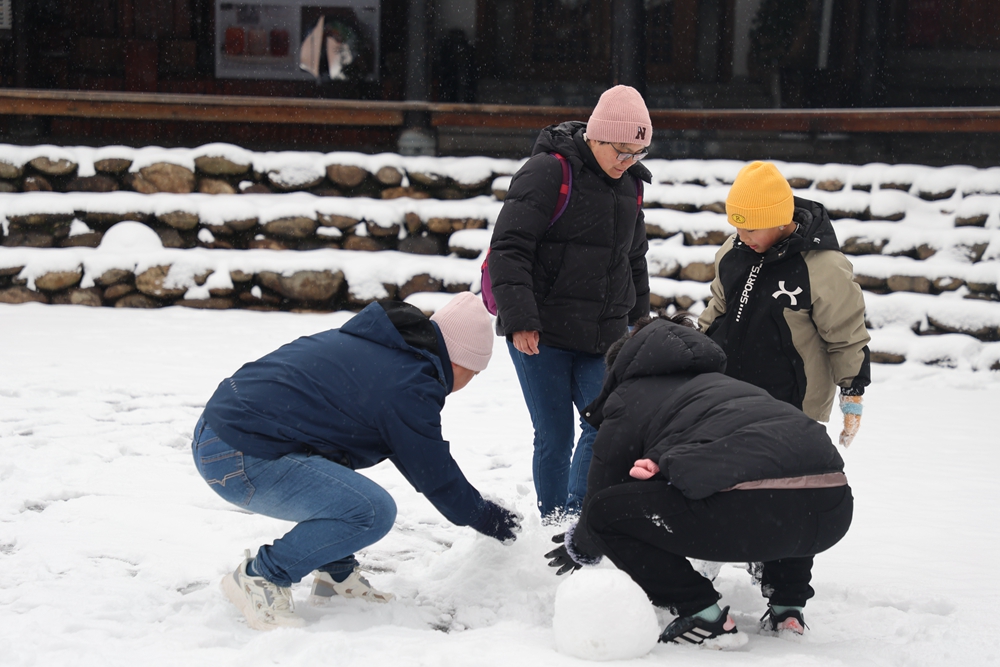 貴州雷山西江千戶苗寨迎來降雪  冬日雪景如畫_fororder_1月22日，貴州省雷山縣西江千戶苗寨迎來2024年第一場降雪。圖為遊客在蹲雪人。