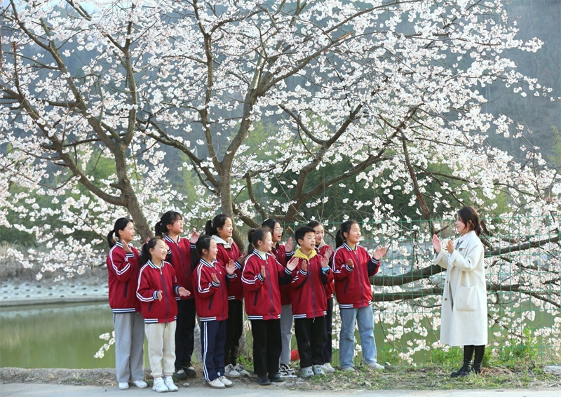 【春日“豫”新景】信陽商城：山花爛漫迎春來_fororder_學生假日春遊，桃花樹下傳笑語。遊家明 攝 - 復件(1)