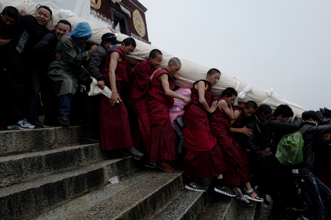 Les moines du monastère de Drepung portent un thangka roulé pour célébrer le début du Shoton, le mot tibétain pour le festival annuel du yaourt d'une durée d'une semaine, à Lhassa, capitale de la région autonome du Tibet (sud-ouest de la Chine), le 11 août 2018. Déroulée, l'image religieuse mesure 40 mètres de long et 37 mètres de large. (Phurbu Tashi / Xinhua)