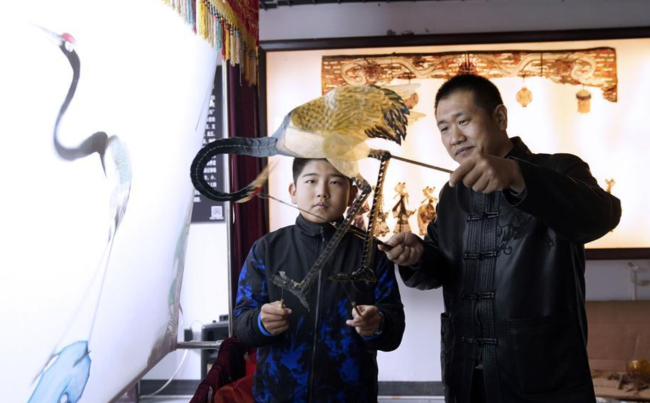 Guo Bao (r.) lehrt ein Kind in seinem Museum, Schattenpuppenspiele zu spielen.