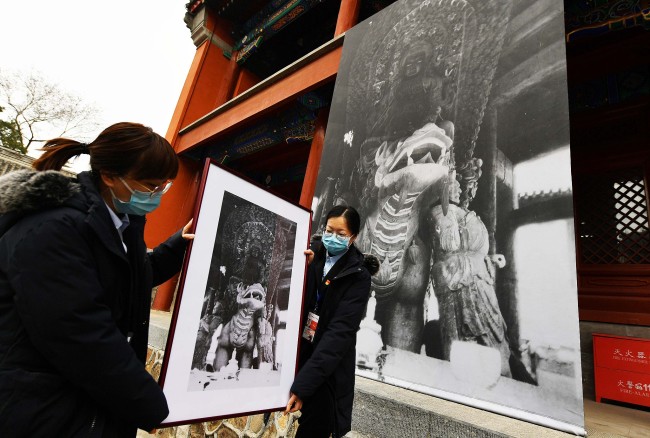 Deux employées du parc Yuanmingyuan présentent une photo prise dans les années 1920 montrant la statue du Bodhisattva Wenshu du temple Zhengjue.(Photo/CFP)