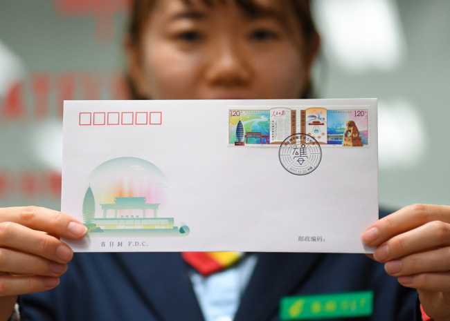Une employée de la poste montre les timbres commémoratifs pour l'établissement de la Nouvelle Zone de Xiongan estampillés sur une enveloppe, dans le district de Xicheng à Beijing, le 22 décembre 2017. [Photo / Xinhua]