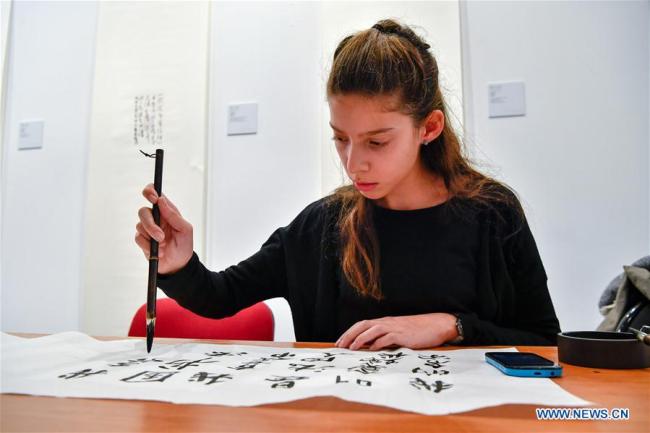 Une jeune femme s'essaie à la calligraphie chinoise au siège de l'UNESCO à Paris, en France, le 11 décembre 2017. Environ 50 pièces du calligraphe chinois Zhang Xuguang y sont présentées. (Chen Yichen)