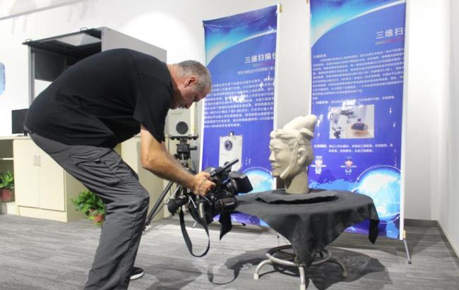 Un journaliste étranger filme devant la tête d’une statue de guerrier de Qin imprimée en 3D