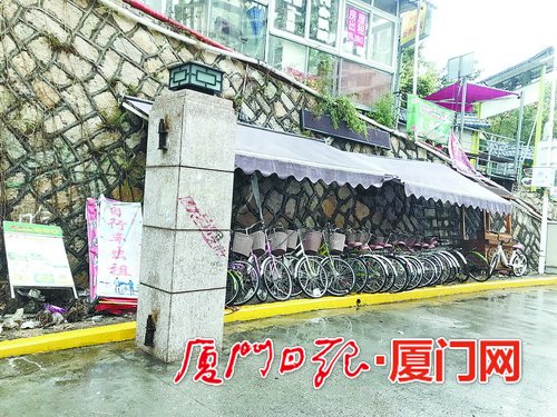 【法治 主推】【滾動新聞】【地市 廈門】(摘要：記者來到廈大芙蓉隧道出口黃女士所説的自行車棚附近。發現設置在一處斜坡石壁下的紫色車棚已微微泛白，十幾輛自行車歪歪斜斜地停在棚內，一旁寫有“自行車出租”的廣告牌倒在地上。走近一看，車把手、座椅上都覆蓋了一層灰，車身銹跡斑斑，車輪裏還有不少零食包裝袋和紙杯。)廈大芙蓉隧道出口自行車棚無人管 人行道垃圾成堆